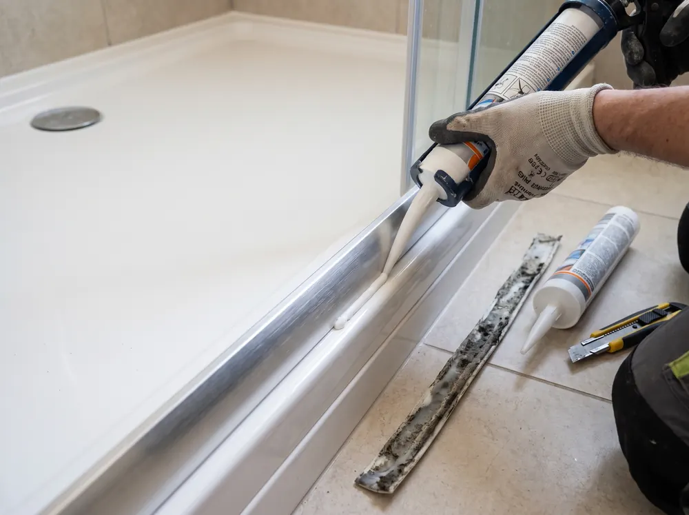 Técnico a aplicar silicone novo na junta entre a base de duche e a calha da cabine